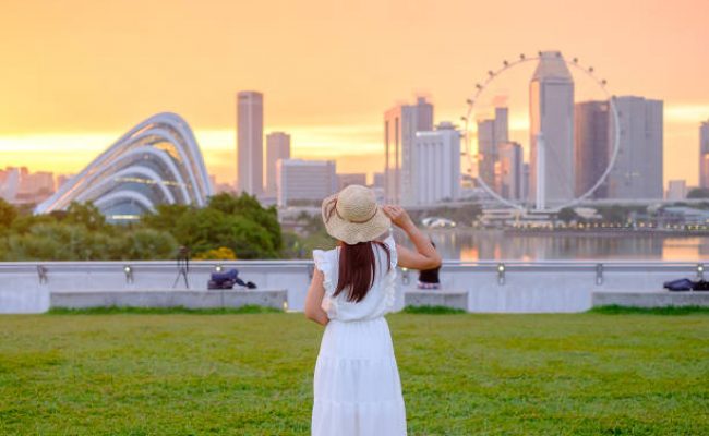 Young Woman traveling with hat at Sunset, happy Asian traveler visit in Singapore city downtown. landmark and popular for tourist attractions. Asia Travel concept