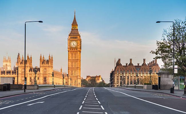 The Houses of Parliament, the Big Ben and Westminster Bridge in London at dawn. Available space for copy on the sky and on the empty road.