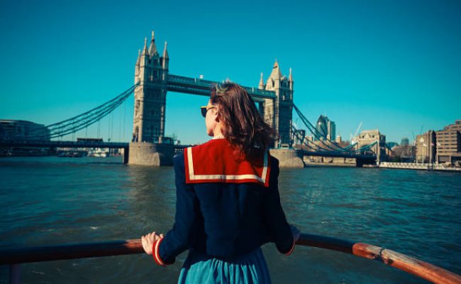 A young woman on a boat is looking at Tower bridge and the London skyline