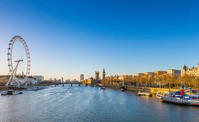 London's skyline view at sunrise with famous landmarks, Big Ben, Houses of Parliament and ships on River Thames with clear blue sky - London, UK